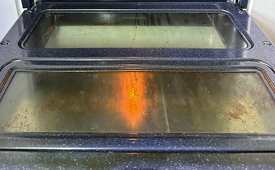 Oven door glass before cleaning - showing grease and grime buildup